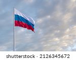 Waving Russian flag against a blue sky with clouds and empty space for text. Room for text. National flag of the Russian Federation.
