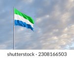 Waving Sierra Leone flag against a blue sky with clouds and empty space for text. Room for text.