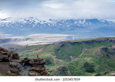 Waving tourist on cliff with canyon and mountains in background. Young man with spreaded hands waving on the rock with abyss under him. Human with hands in the air shaking by his arms to photographer. - Powered by Shutterstock