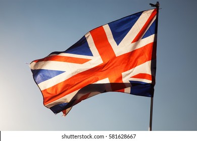 waving UK flag in the blue sky, Union Jack flag - Powered by Shutterstock