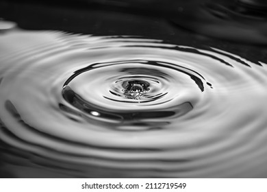 Wavy circles on the water with glare. Black and white photo. Liquid background. Side view close up.