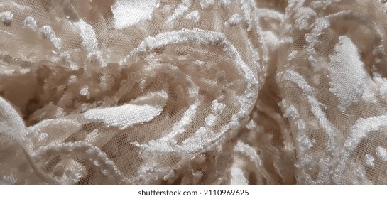 Wavy light beige translucent fabric with a floral screen print and a patterned crescent moon silhouette at the center; in folds (macro, top view, texture).