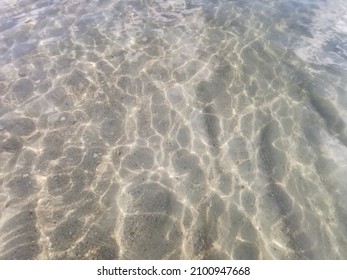 Wavy Natural Sunlight Shine On Crystal Clear Sea Water Body With See Through White Sand Beach In The Background  