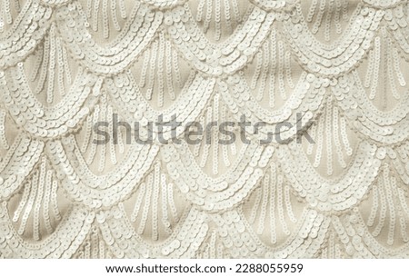 Wavy sequins pattern on white decorative fabric background. Abstract embroidery of small round sequins on clothing material