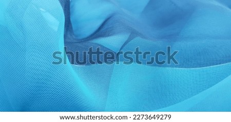 Wavy turquoise blue translucent fabric (chiffon) with a golden thread, in folds (macro, texture).
