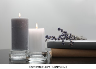 Wax candles in glass holders near books and lavender flowers on table against light background