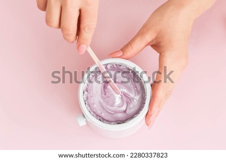 Wax melter, wax heater, wax melting device on a pink background. Salon equipment. Wooden spatula in female hands. Pink wax. Top view. Close up