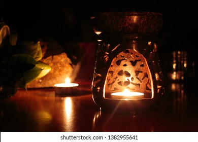 Wax Warmer, Wax Melt, Warmer Candle With Candle Light Inside. Picture Was Took With Natural Light From The Fire. In The Background Are Stone And Plant.