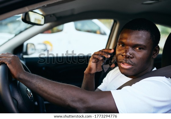 Waxed African appearance with a mobile phone at the\
wheel of a car