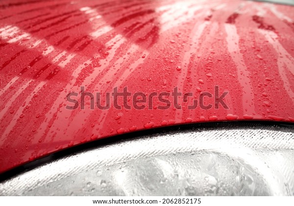 Waxed car hood after rain. Visible\
water droplets and traces of run-off over the lights.\
