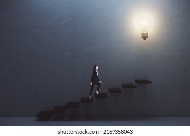Way to success and creative idea concept with young woman climbing the stairs to big illuminated light bulb on dark grey wall