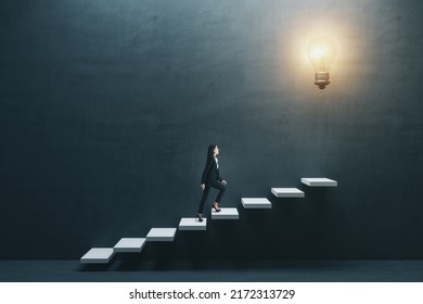 Way to success and creative idea concept with young woman climbing white stairs to big illuminated light bulb on dark grey wall