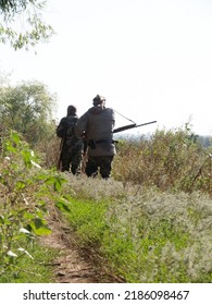 Ways To Carry Rifles. A Hunters With A Rifles Walks Along A Country Road. One Of Them Has A Rifle Hanging On His Shoulder, And The Other One Has It On The Neck In Front.