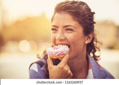 We All Deserve A Day Of Indulgence. Young Woman On City Street Eating Donut. Close Up. Copy Space.