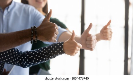 We all say yes! Close up shot of four young people workers clients of different gender ethnicity raising thumbs up showing general support acceptance recognition to company policy, service or product