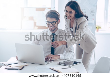 We already have great results! Young beautiful woman pointing at laptop with smile and discussing something with her coworker while standing at office 
