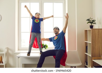We can do it. Happy young dad and active kid dressed as superheroes enjoying time together. Funny father and child in super hero cloaks playing games at home. Fun childhood, parents' support concept