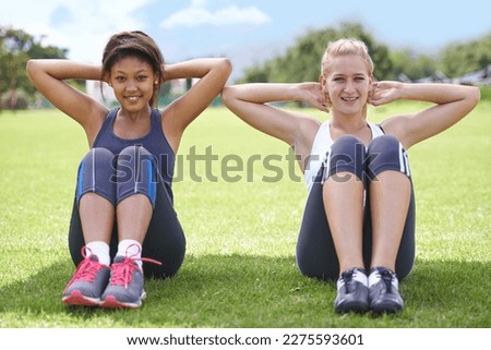We can do it. young women doing sit ups on the grass outside.