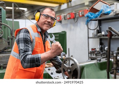 We can do it - Powerful young industrial worker man in a success pose. Confident worker wearing protective gear and ear defenders while operating machinery in a factory. - Powered by Shutterstock