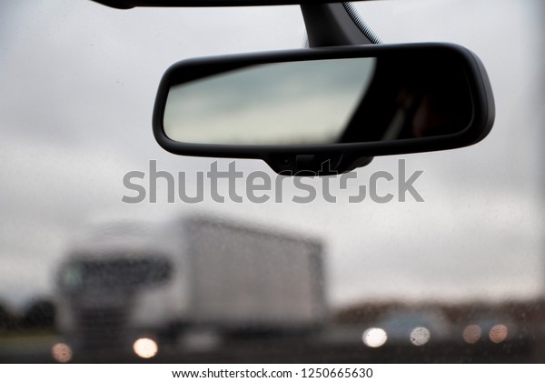 We can see a rear view mirror from a car\
moving on an highway, the background is blurry, we can see the cars\
going the other way in the\
background