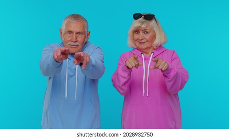 We choose you. Elderly woman granny with man grandfather pointing to camera looking with happy expression, making choice, showing direction. Senior grandmother with grandpa isolated on blue background