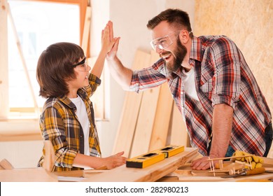 We did it! Cheerful young male carpenter and his son giving high-five to each other while working in workshop - Powered by Shutterstock