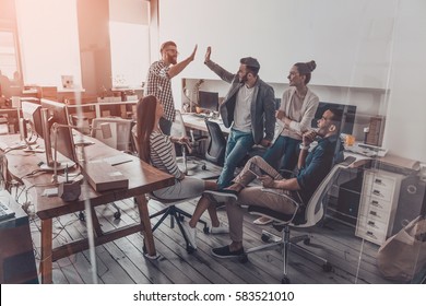 We did it! Two cheerful young business people giving high-five while their colleagues looking at them and smiling  - Shutterstock ID 583521010