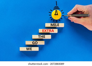 We Go The Extra Mile Symbol. Wooden Blocks With Words We Go The Extra Mile. Light Bulb Icon. Businessman Hand, Pen. Blue Background, Copy Space. Business, We Go The Extra Mile Concept.