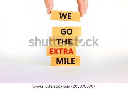 We go the extra mile symbol. Wooden blocks with words We go the extra mile. Beautiful white background, copy space. Businessman hand. Business, we go the extra mile concept.