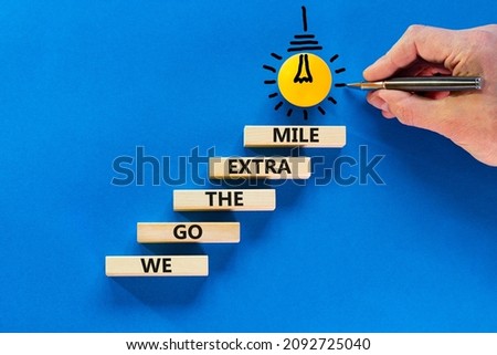 We go the extra mile symbol. Wooden blocks with words We go the extra mile. Light bulb icon. Businessman hand, pen. Blue background, copy space. Business, we go the extra mile concept.