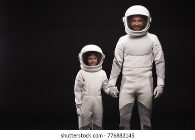 We are good team. Portrait of cheerful father standing hand by hand with his little son. They are wearing hyperbaric astronaut protective suit and looking at camera with joy. Isolated with copy space