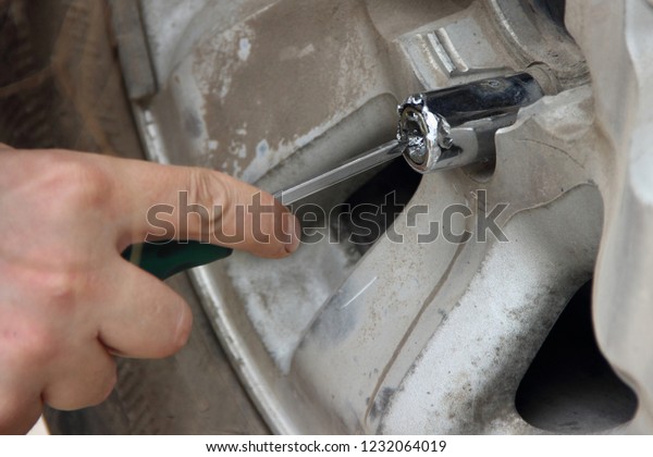 We got a flat tire - man hands unscrews the\
secret nut on the spare wheel - breaks the lock with a screwdriver,\
hand tool closeup