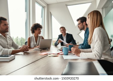 We have great results. Multicultural team discussing new project and smiling while sitting at the office table - Shutterstock ID 1503920270