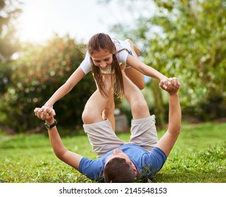 We Have Lift Off. Shot Of A Father Lifting Up His Daughter With His Legs While Lying On The Grass Of A Park Outside During The Day.