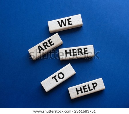 We are here to help symbol. Concept words we are here to help on wooden blocks. Beautiful deep blue background. Business and we are here to help concept. Copy space.