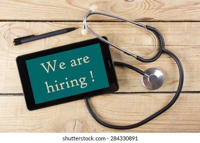 We Are Hiring !  - Workplace Of A Doctor. Tablet, Medical Stethoscope, Black Pen On Wooden Desk Background. Top View