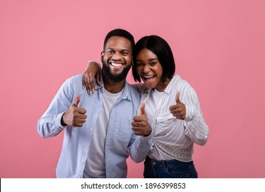 We like it. Happy black couple showing thumbs up gesture, approving or recommending something over pink studio background. Positive millennials expressing their agreement
