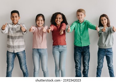 We Like It. Happy Multiethnic Kids Gesturing Thumbs Up Approving School Education Offer Posing Smiling To Camera Standing Together Near Gray Wall Indoor. Approval Concept - Powered by Shutterstock