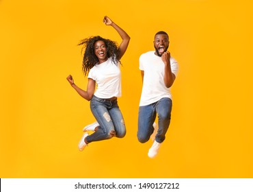 We made it. Joyful Afro Couple Jumping Up And Down, guy clenching his fist, yellow studio background