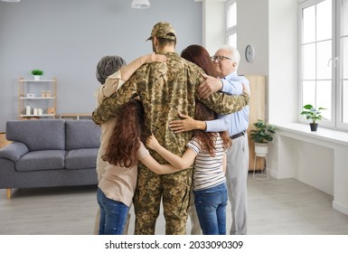 We Missed You So Much. Family Reunited With Veteran Father Who's Returned Home From Military Service. Back View Portrait Happy Young Soldier In Camo Uniform Standing In Living Room And Hugging Family