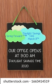 We Open At 9 O'clock Spring Forward Daylight Savings Time March 8 Blackboard Sign Hanging On Wood Grain Door