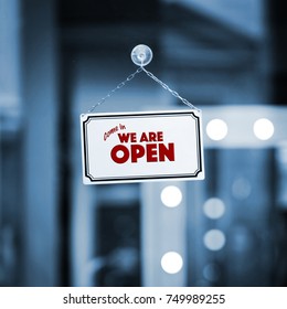 WE ARE OPEN sign board through the glass of store window. Filtered image. - Shutterstock ID 749989255