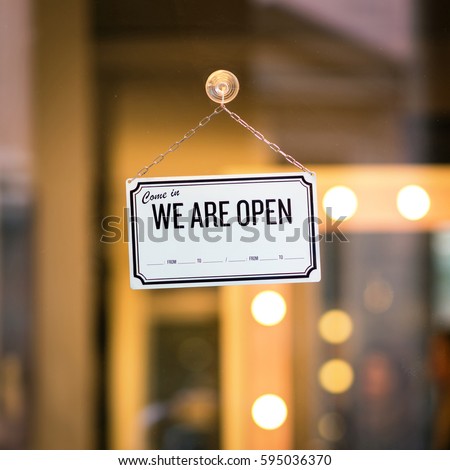 WE ARE OPEN sign board through the glass of store window. Filtered image.