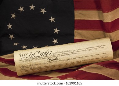 We The People, The Opening Words Of The Preamble To The Constitution Of The USA, Is Prominent On The Copy Of The Constitution. The Parchment Document Is Lying On An Aged Colonial Era American Flag. 