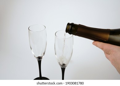 We Pour Champagne Into Glasses On A White Background. A Hand And Champagne Bubbles Are Visible.