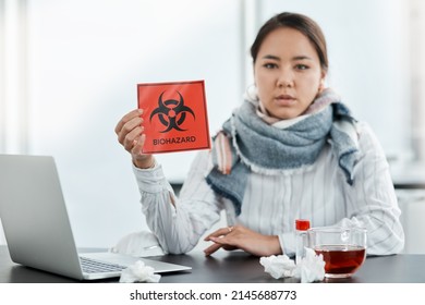 We Should All Be Safety Conscious During This Crisis. Shot Of A Young Businesswoman Holding A Biohazard Sign At Her Desk In A Modern Office.