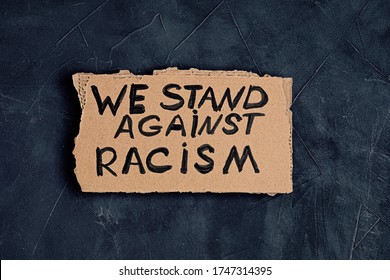 We stand against racism text on cardboard over dark background