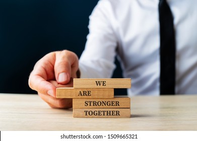 We Are Stronger Together Sign On Wooden Pegs Being Stacked By A Business Executive In A Conceptual Image. Over Dark Blue Background.