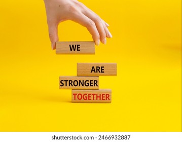 We are stronger together symbol. Wooden blocks with words We are stronger together. Businessman hand. Beautiful yellow background. We are stronger together concept. Copy space.