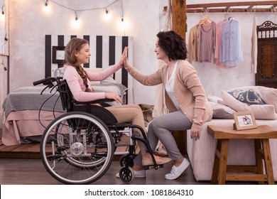 We team. Positive girl with a disability and woman posing in profile while exchanging high five - Powered by Shutterstock